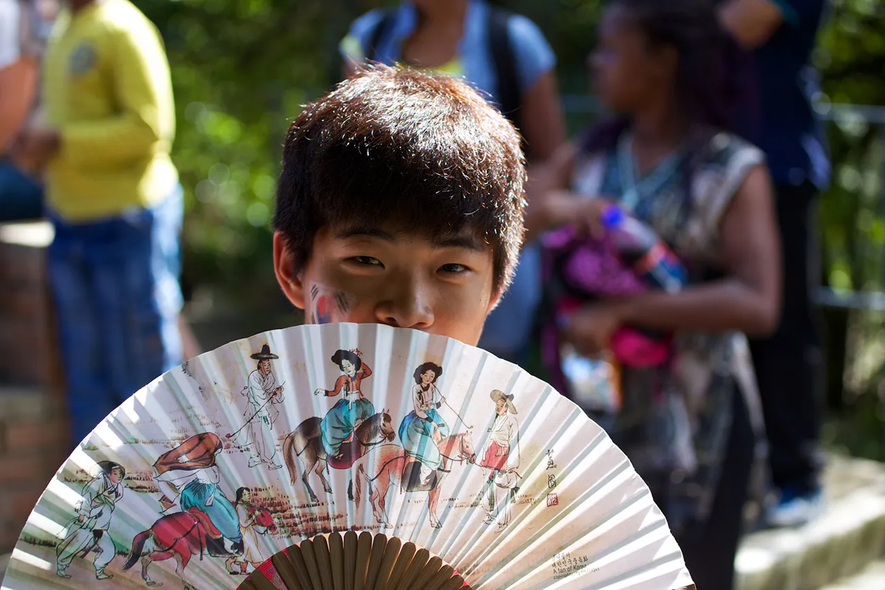 A boy is covering a part of his face with a fan